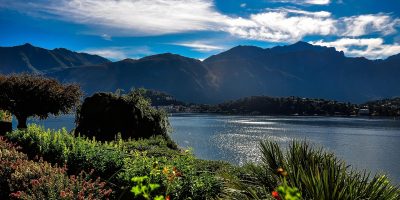 科莫湖贝拉焦小镇全景，湖面倒映山色，彩色建筑沿湖而建，游船缓缓驶过